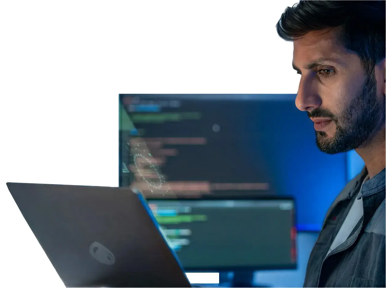 IT professional working on a laptop in front of monitors showing code