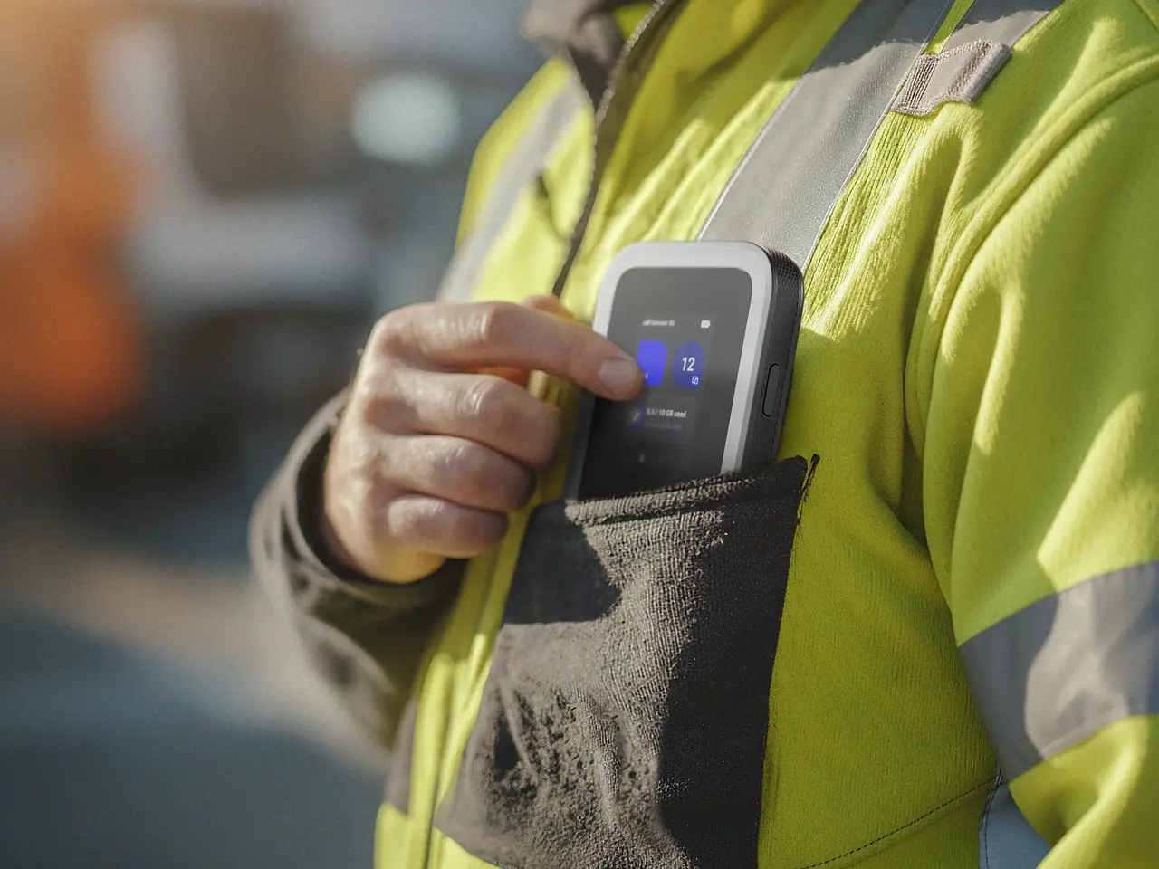 Worker in a high-visibility jacket pulling a Nighthawk mobile hotspot from a chest pocket