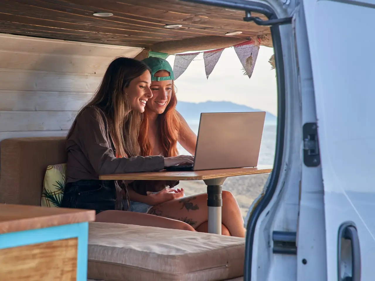 Two friends using a laptop inside a camper van parked by the beach